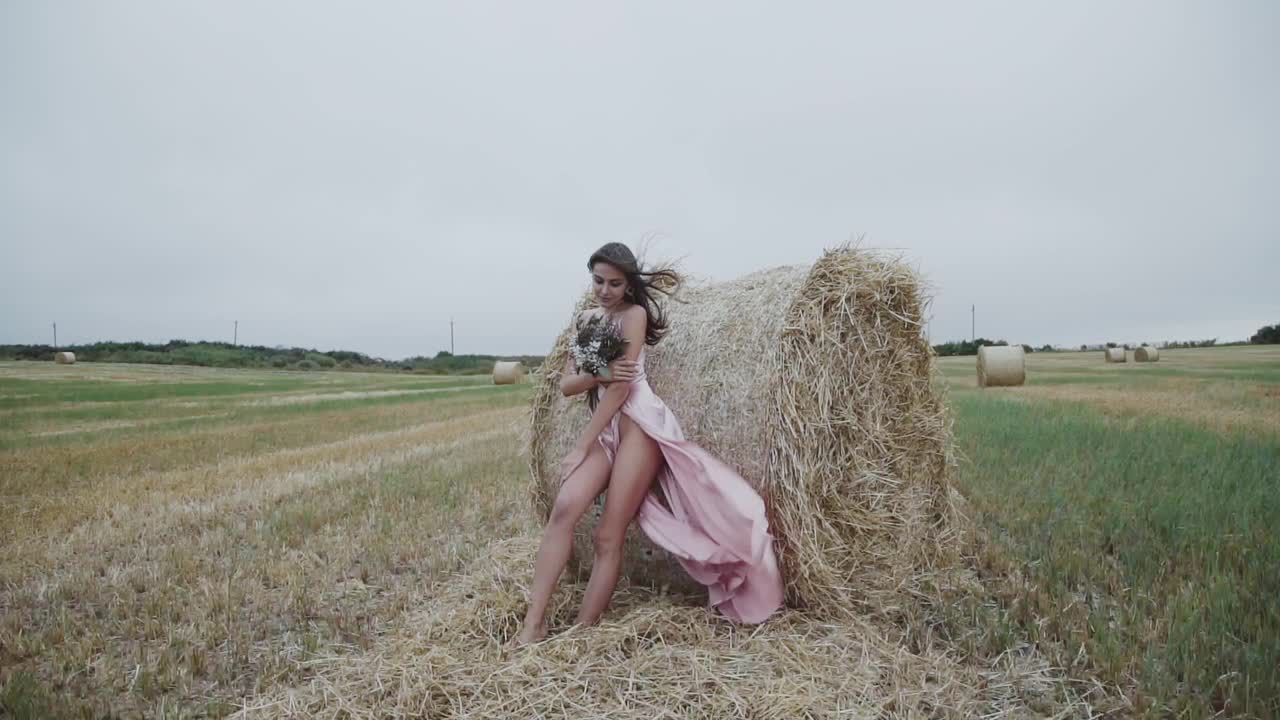 漂亮的女士在吹晚礼服和花束站在干草堆姿势视频素材