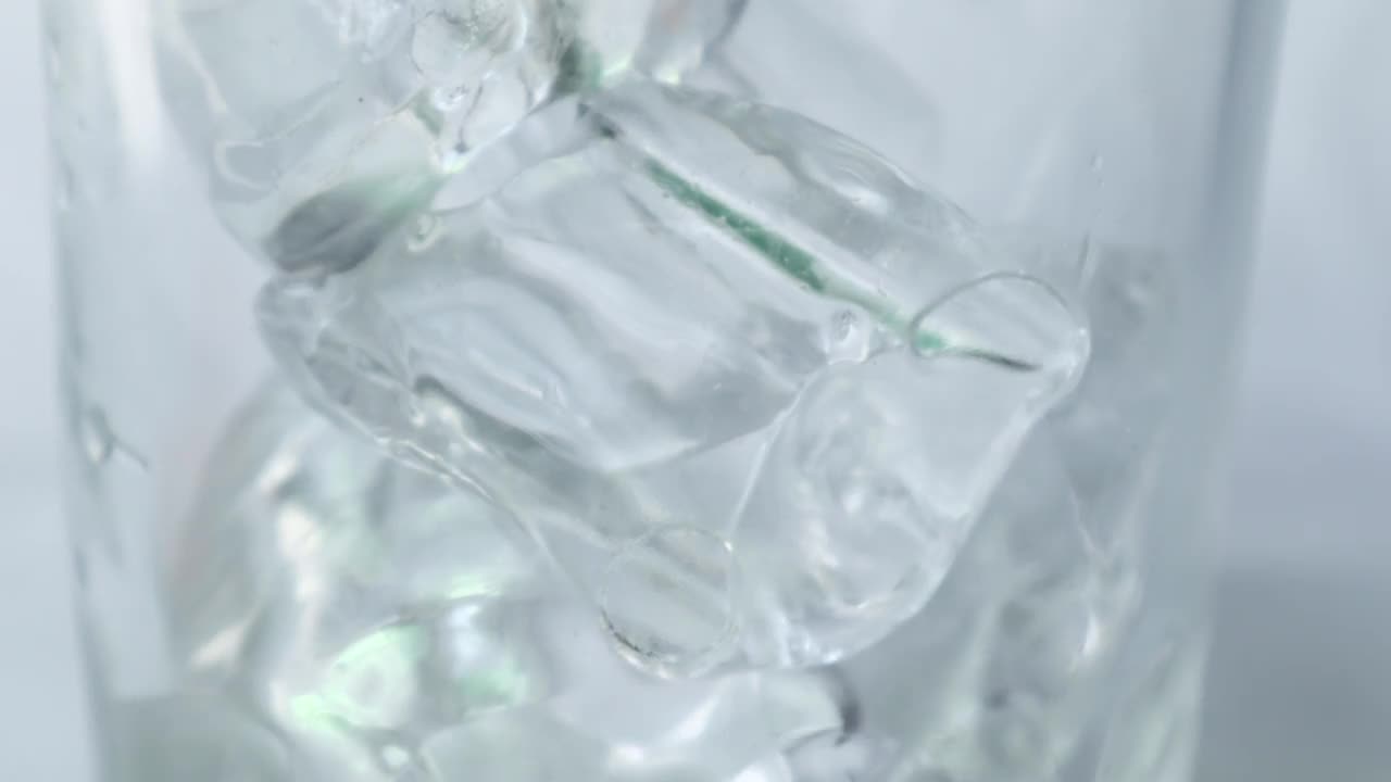 用慢动作将水倒入装有冰块的玻璃杯中。视频素材