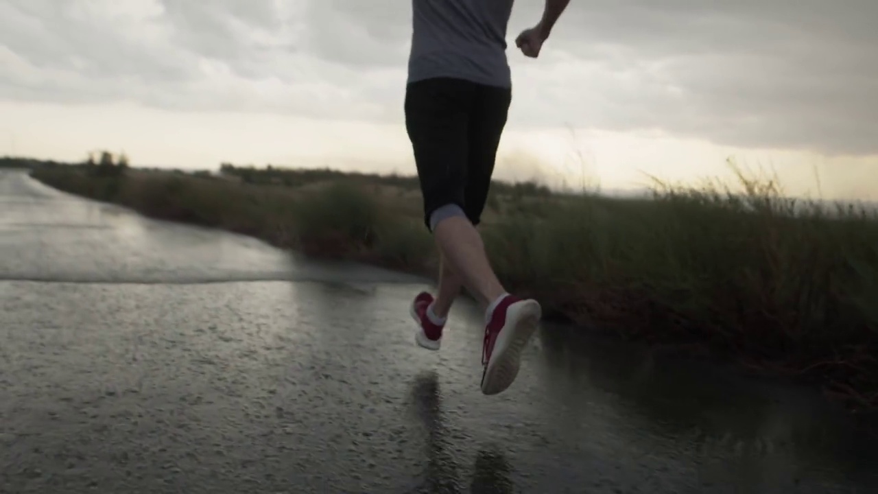 体格健壮的男子在阴沉沉的灰色天空和田野的背景下，在雨中奔跑，向后向下看。体育动机视频素材