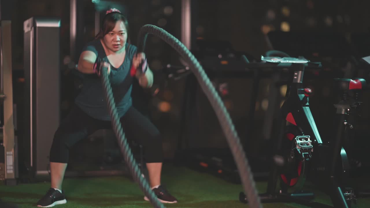 身体积极的亚洲华人中年妇女晚上在健身房练习战斗绳视频素材