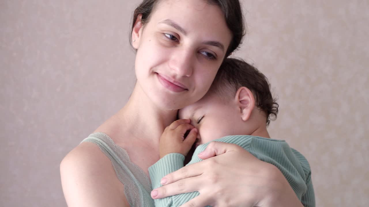 母亲抱着熟睡的儿子在家里摇晃。男孩睡在母亲的怀里视频素材
