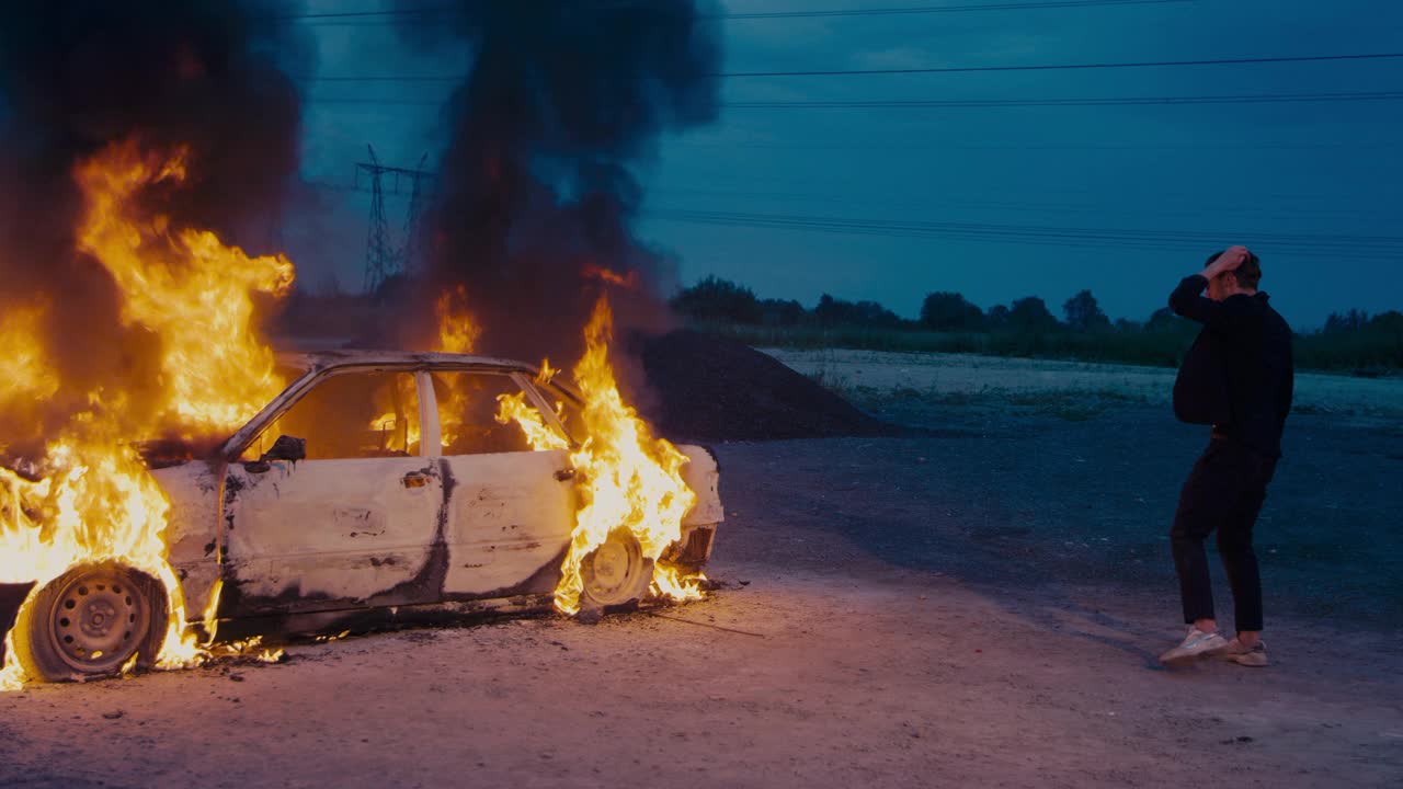 一个穿着西装的欧洲人走过一辆燃烧的汽车。视频素材