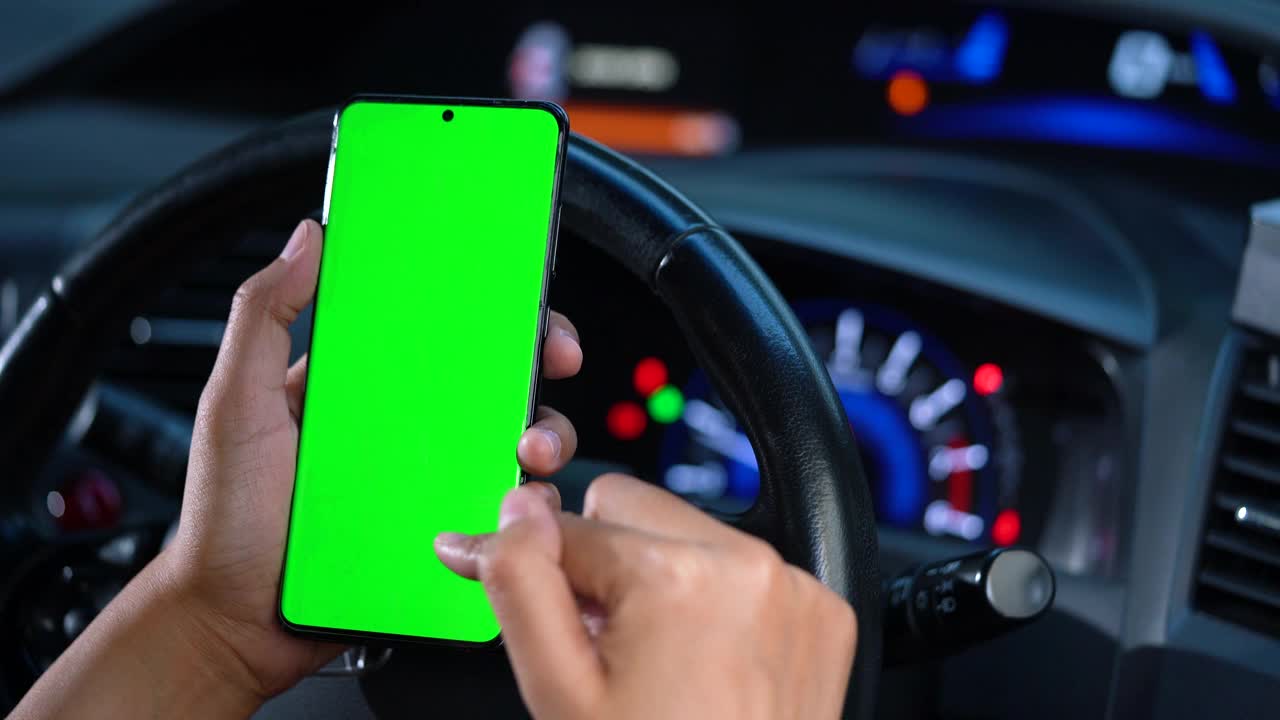 在电动汽车中，女性手持智能手机，智能手机上有绿色的空白屏幕，用于导航、按摩、定位和商务。女性坐在现代电动汽车里，用智能手机工作——绿色屏幕——特写。色度键。视频下载
