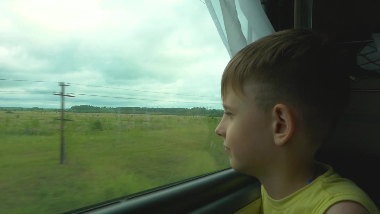 6-8岁的白人男孩坐在火车上看着窗外，挥手示意。这个孩子乘火车去度假。火车上的男孩望着窗外，微笑着挥手。视频下载