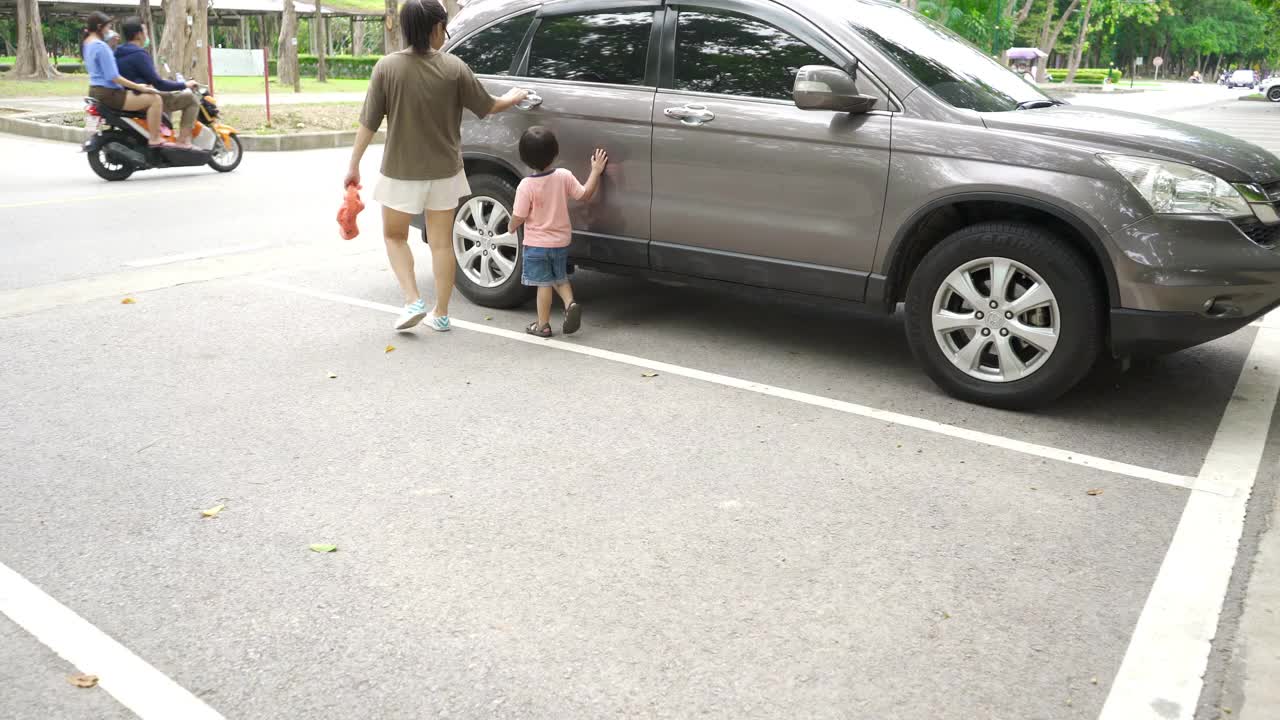 一个蹒跚学步的小男孩和他的妈妈在公园玩完后正走向一辆汽车视频素材