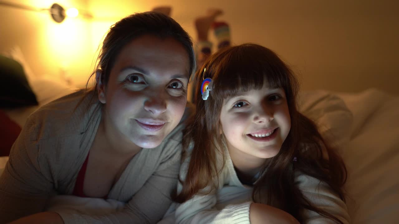 母亲和女儿躺在家里的床上用电子平板电脑看东西视频素材