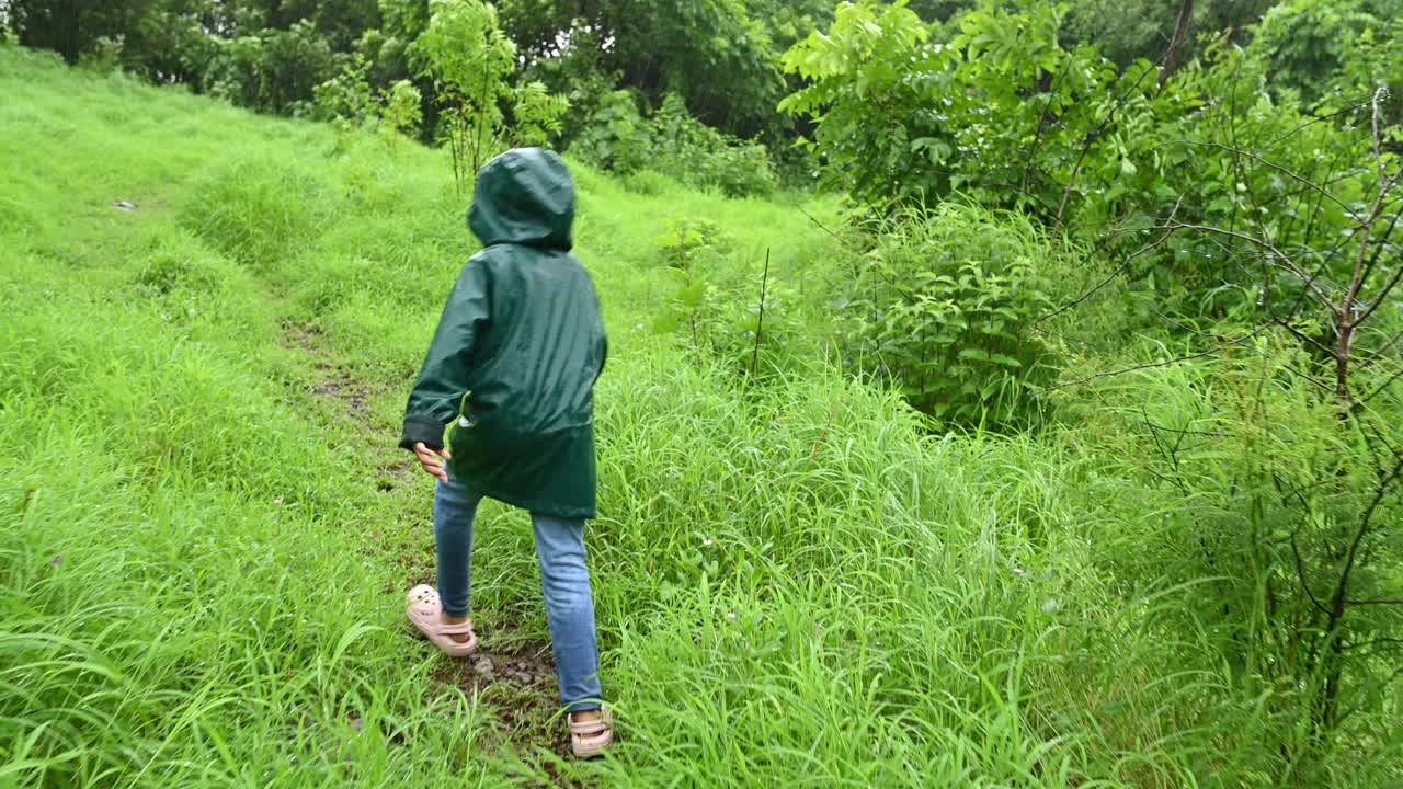 一个穿着雨衣的小女孩在雨中徒步的后视图视频下载