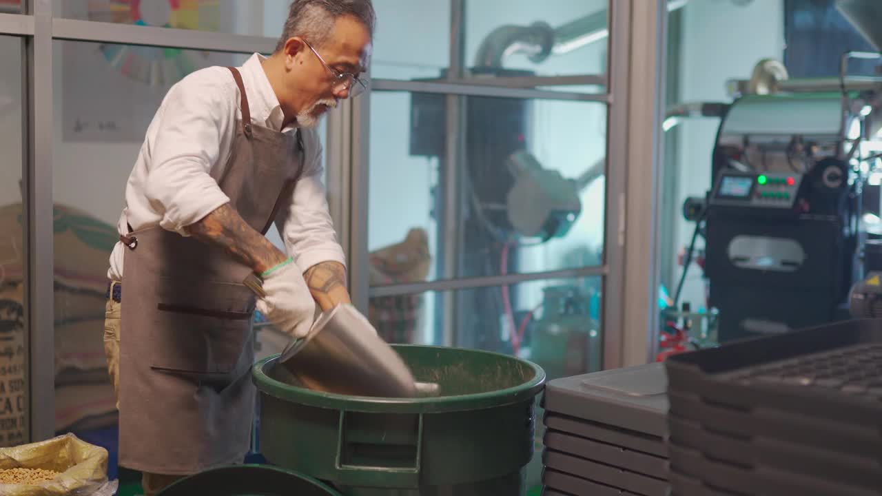 亚洲华人技工将生咖啡豆从桶中舀到秤机上，并将其混合在工厂仓库的咖啡烘焙过程中视频下载