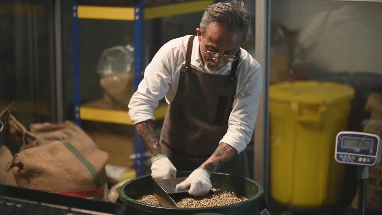 亚洲华人高级技工将生咖啡豆从桶中舀到秤机上，并将其混合在工厂仓库的咖啡烘焙过程中视频素材