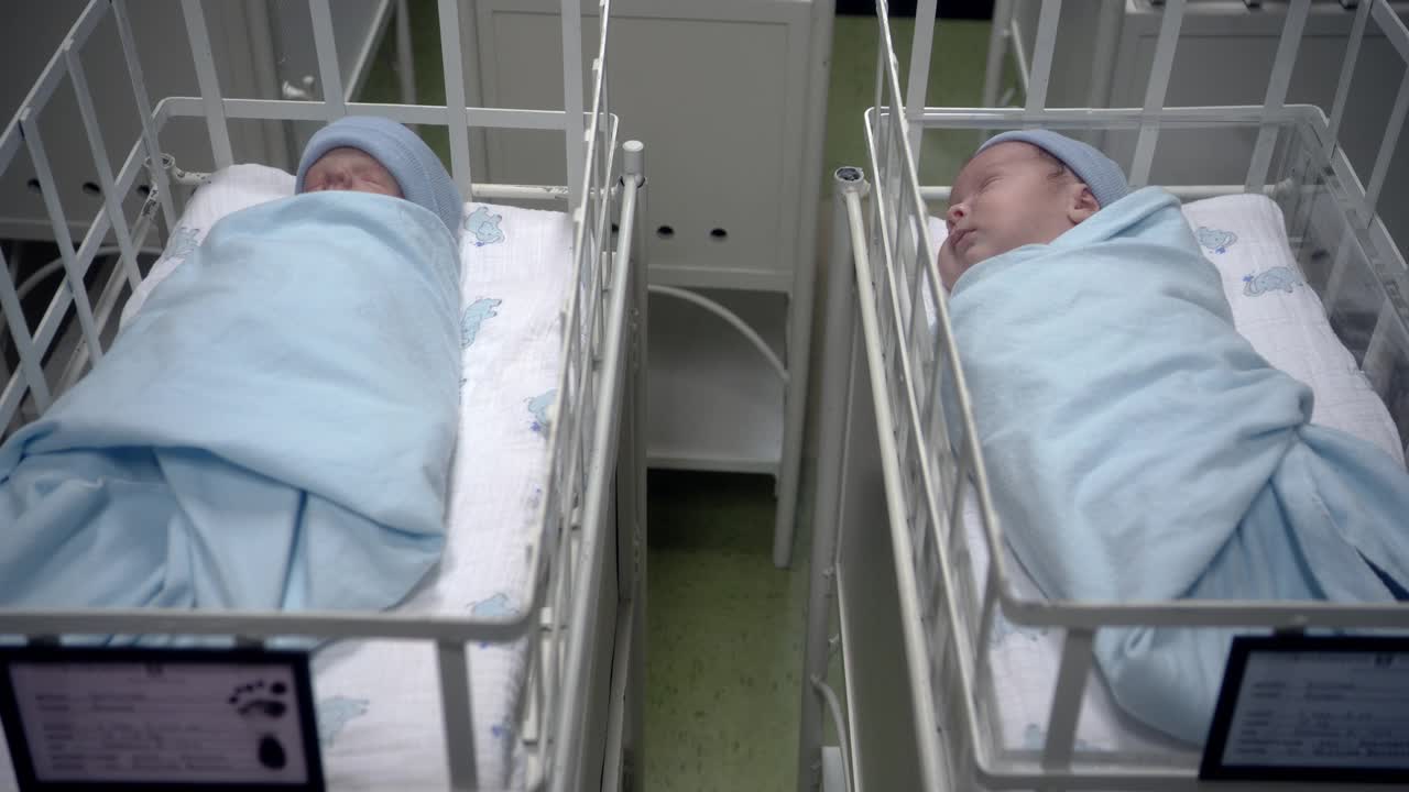 在医院的摇篮里，两个婴儿裹着蓝毯子，戴着蓝帽子。可能是产科病房的婴儿房。视频下载