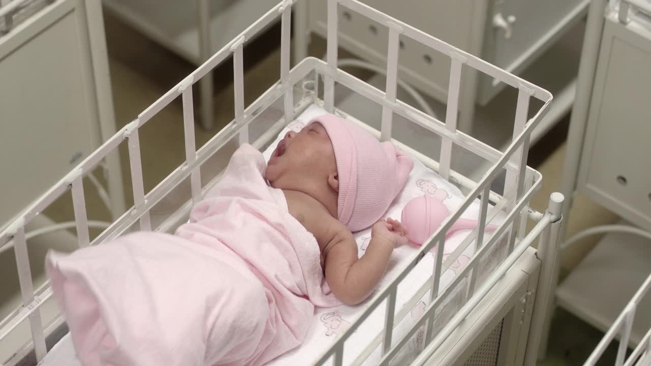 在医院的摇篮里，潘从左到右贴近两个裹着蓝色和粉色毯子、戴着蓝色和粉色帽子的婴儿。可能是产科病房。视频下载