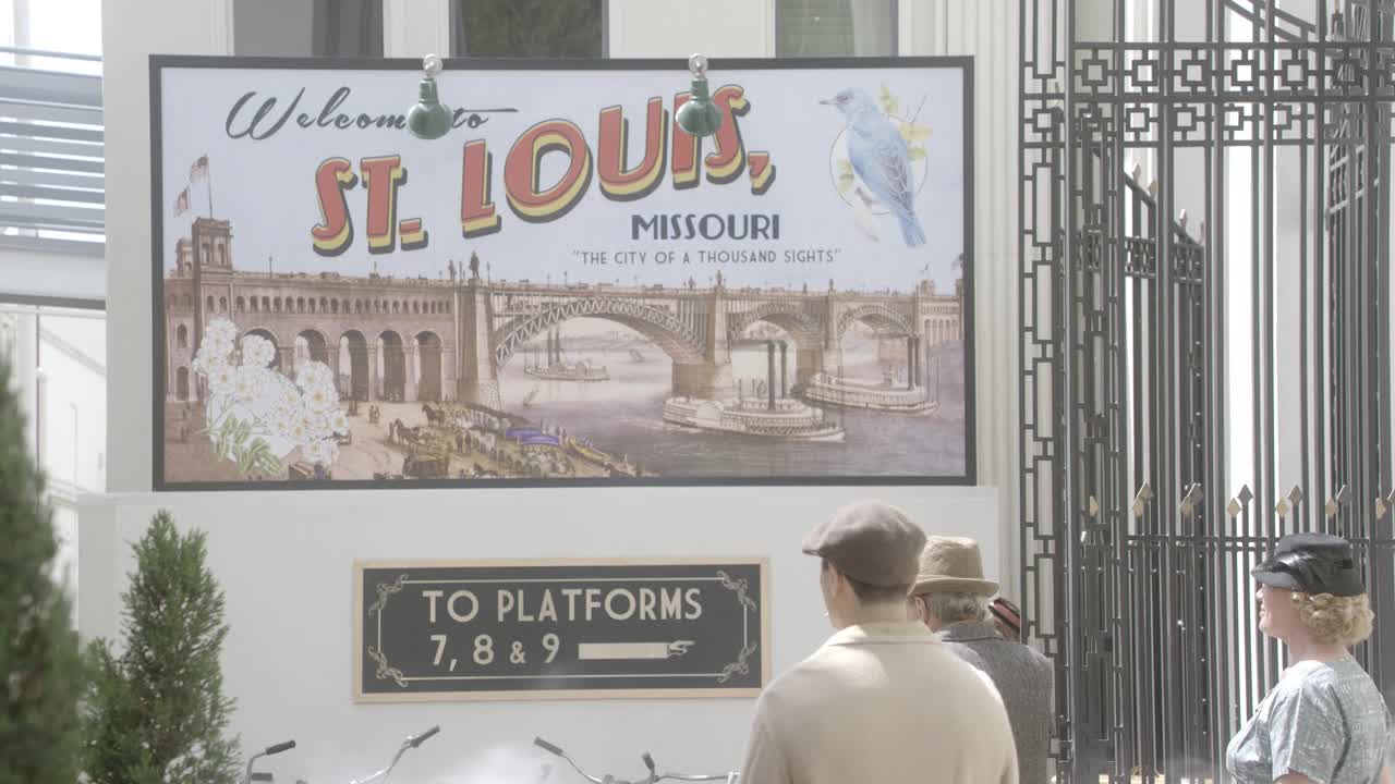 中等角度的标志、广告牌或广告，上面写着“欢迎来到密苏里州的圣路易斯市，千山万水的城市”。可能是一个火车站。旅行者、通勤者和乘客行走可见。从火车上可以看到蒸汽。穿制服的火车搬运工站起来视频下载