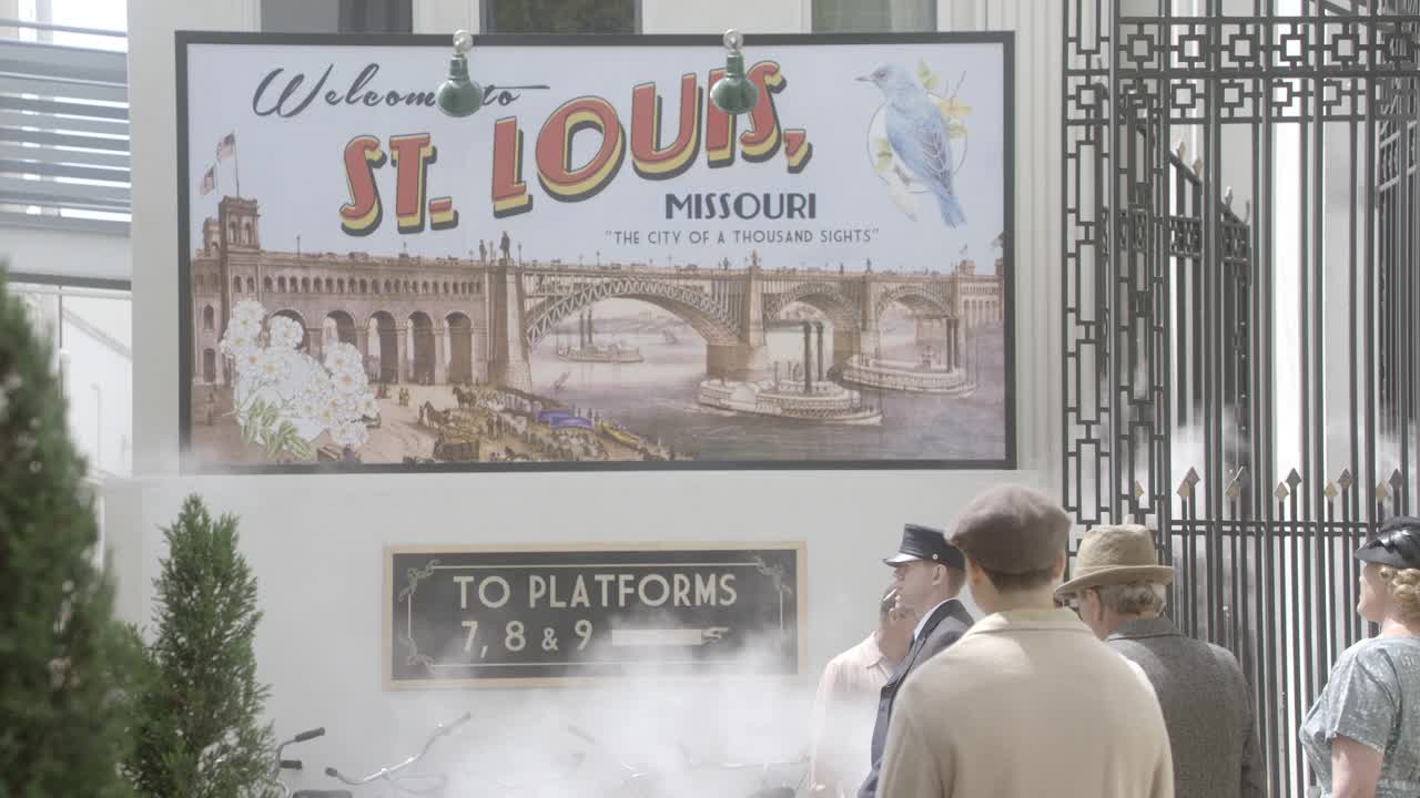 中等角度的标志、广告牌或广告，上面写着“欢迎来到密苏里州的圣路易斯市，千山万水的城市”。可能是一个火车站。旅行者、通勤者和乘客行走可见。从火车上可以看到蒸汽。穿制服的火车搬运工站起来视频下载