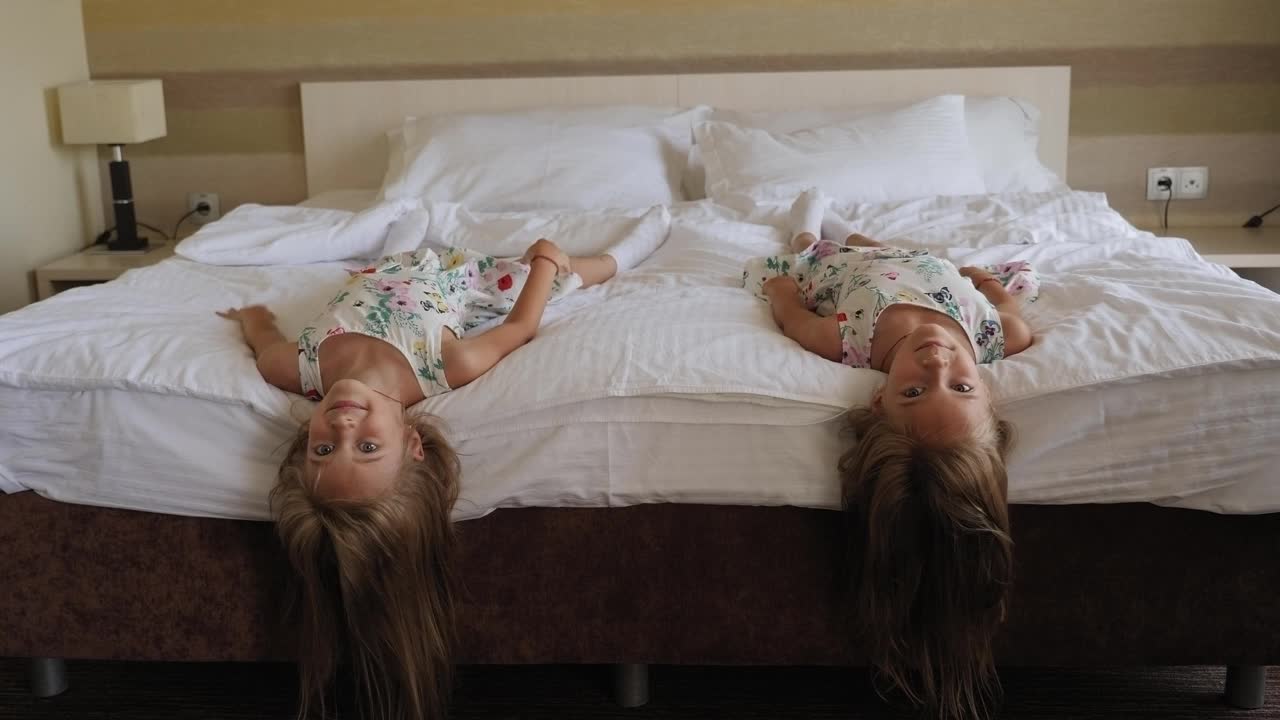 两个穿着相同衣服的双胞胎女孩倒躺在旅馆的床上视频素材