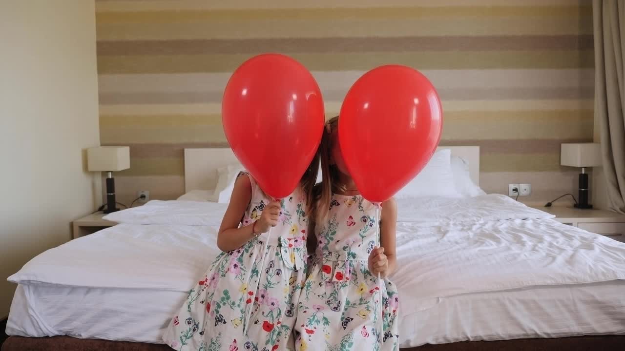 一对双胞胎姐妹坐在挂满红气球的卧室的床上。视频素材