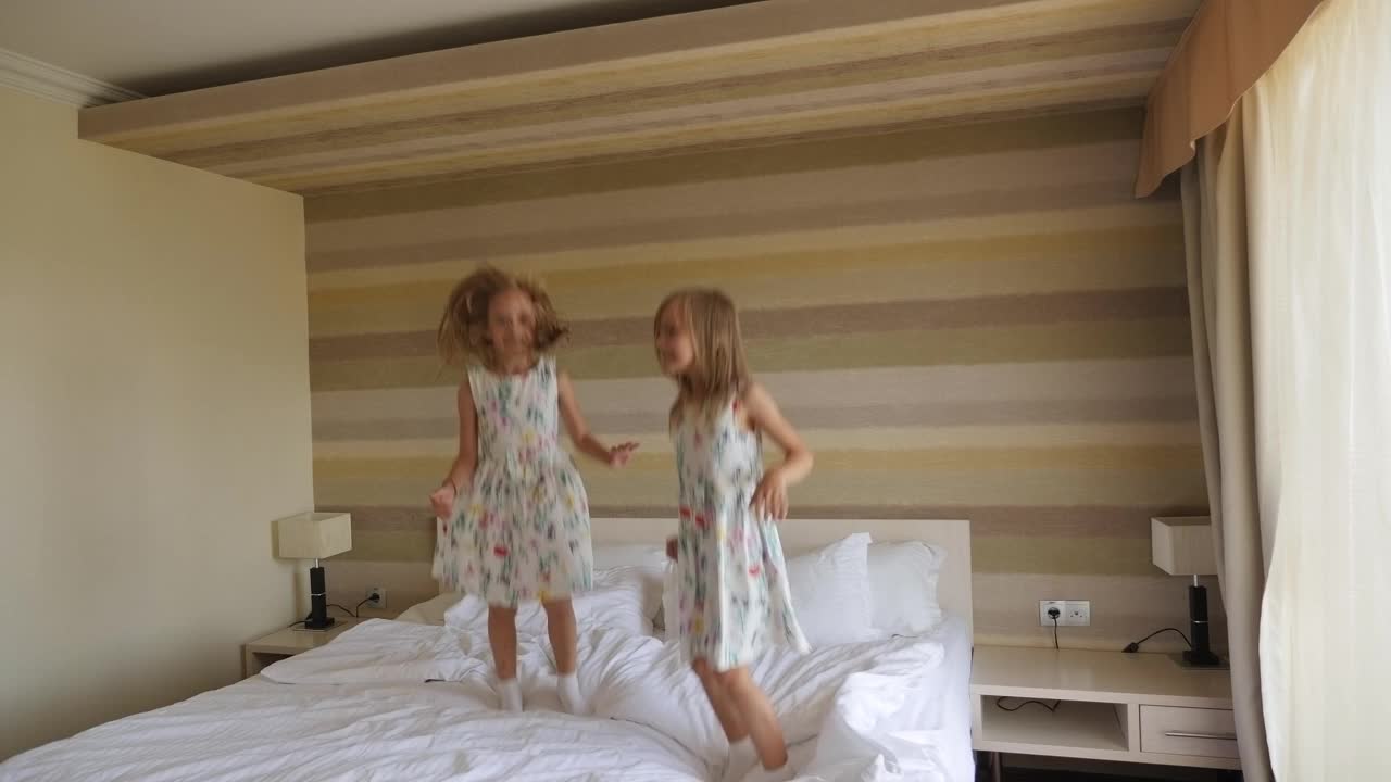 清晨，一对双胞胎姐妹在旅馆卧室的床上跳来跳去。视频素材