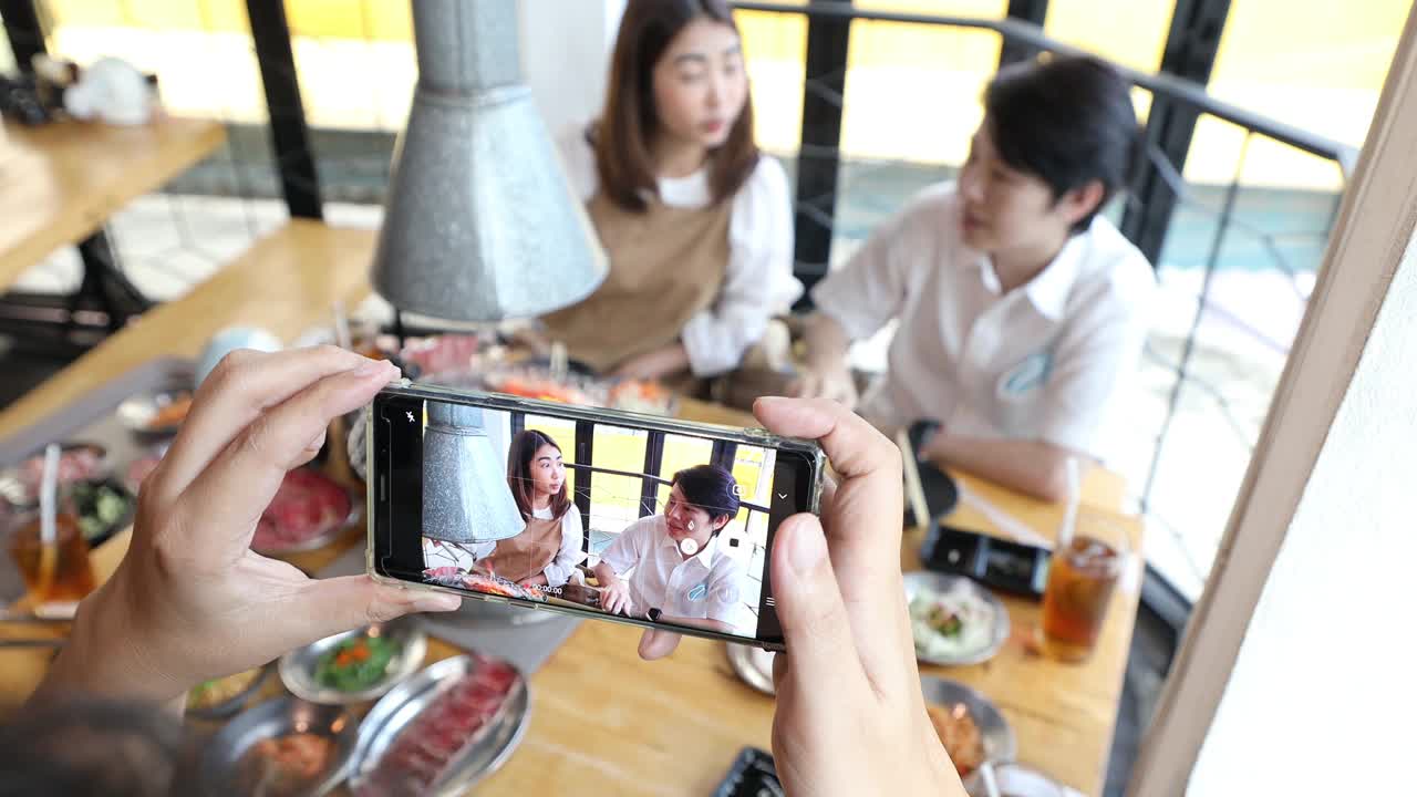 亚洲成年朋友在烧烤餐厅用智能手机拍照和录像视频素材