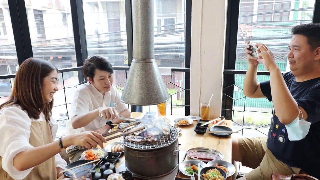 亚洲成年朋友在烧烤餐厅用智能手机拍照和录像视频素材