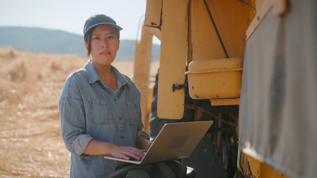女农民使用笔记本电脑旁边的联合收割机在农田视频素材