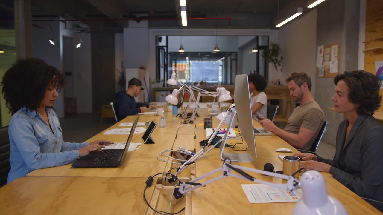一群不同的人坐在他们的办公桌前，一些人专注地工作，另一些人则与他们的同事交谈或交换文件视频素材