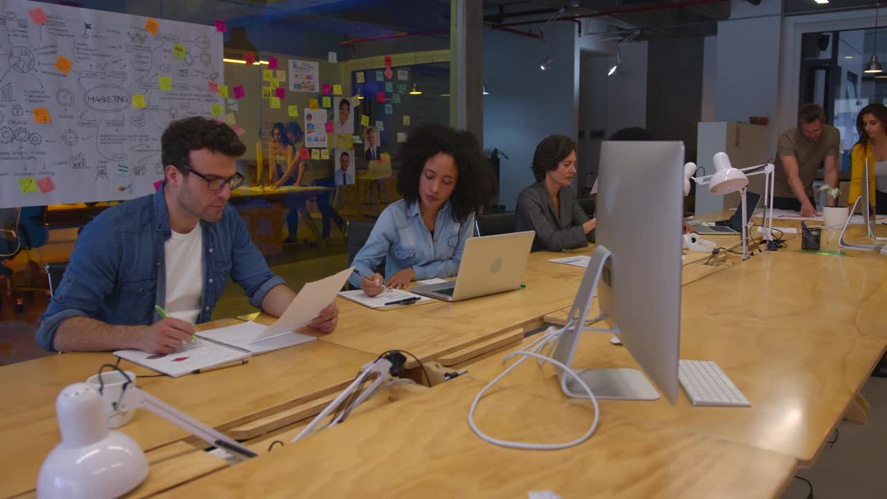 在一家营销机构工作的中等人群，他们坐在办公桌前，有些人和同事一起工作视频素材
