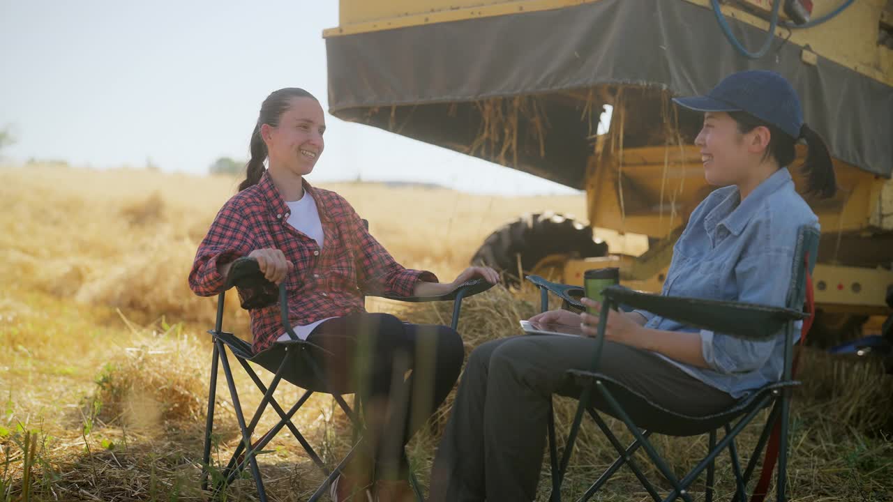 两名多民族女农民在农田联合收割机的阴凉处休息视频下载
