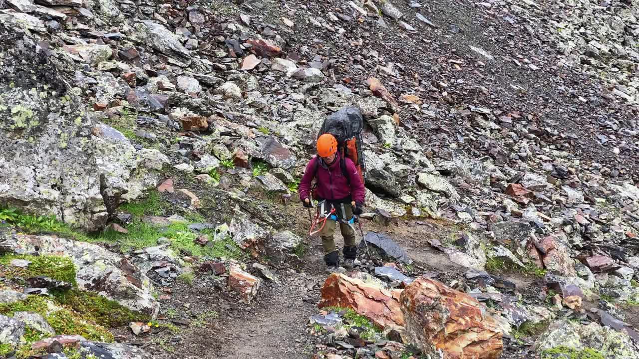 一名戴着橙色头盔、背着大背包的快乐游客走上了山路视频下载