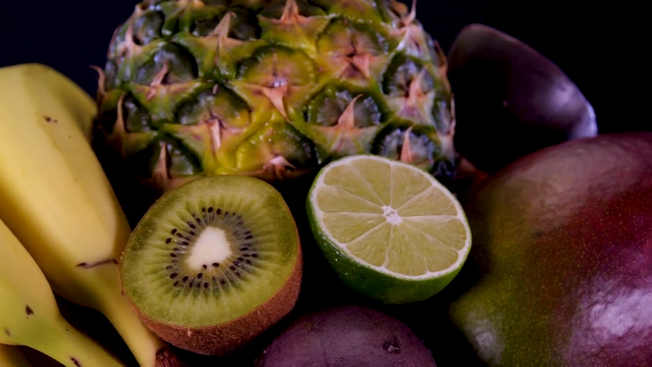 热带和异域水果，菠萝，百香果，猕猴桃，芒果，酸橙，石榴，橘子和香蕉在黑色背景上。夏天水果组成。视频素材