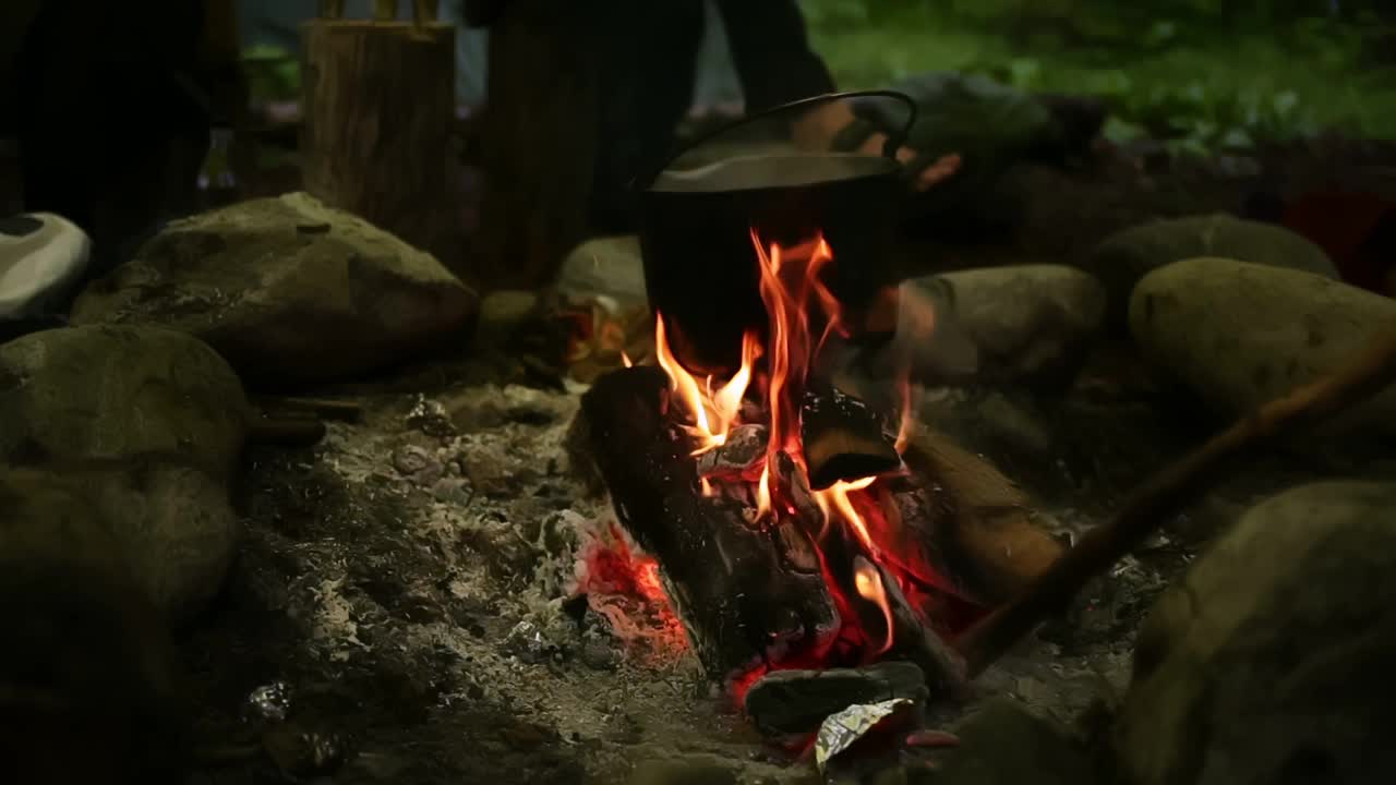 在森林里的篝火旁用水壶煮食物。在高温下烹煮食物。徒步旅行者的特写镜头视频素材