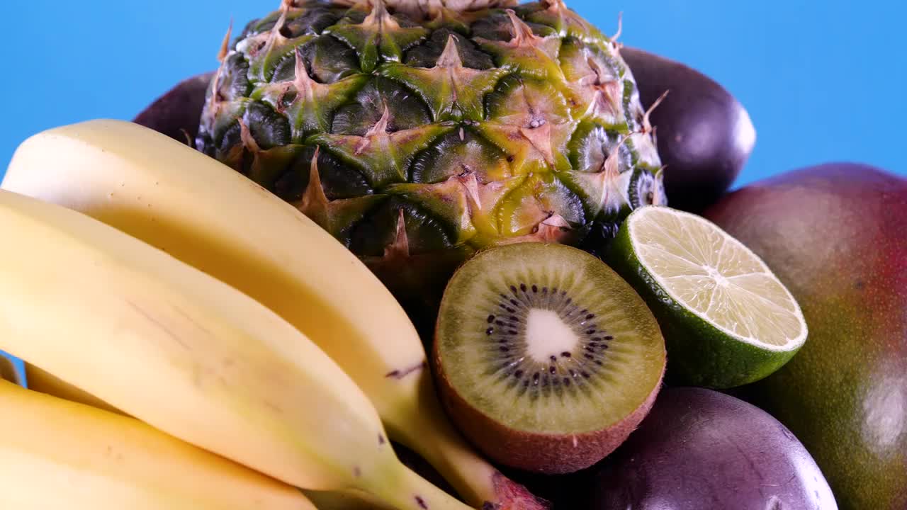 热带和奇异的水果，菠萝，百香果，猕猴桃，芒果，酸橙，石榴，橘子和香蕉在蓝色背景上旋转。夏天水果组成。视频素材