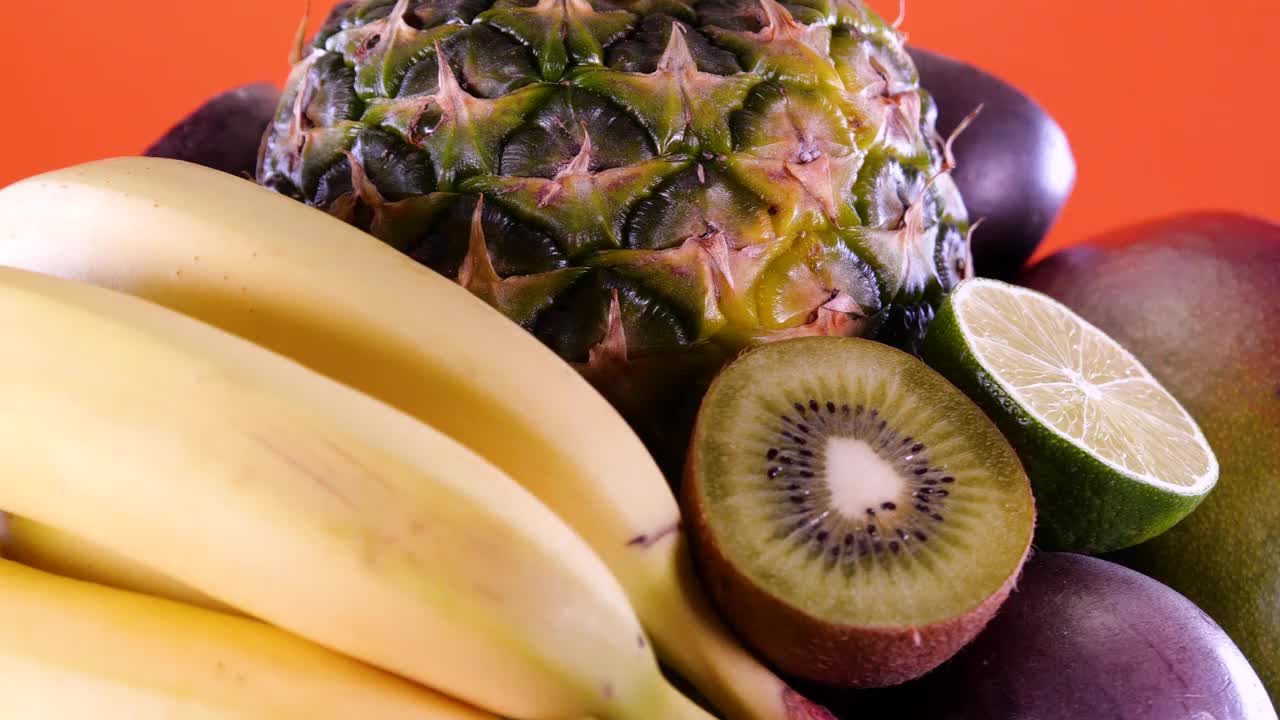 热带和奇异的水果，菠萝，百香果，猕猴桃，芒果，酸橙，石榴，橙子和香蕉在橙色的背景上旋转。夏天水果组成。视频素材