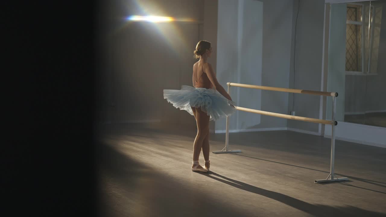 苗条优雅的芭蕾舞女演员在舞蹈室聚光灯下练习踮脚旋转的广角镜头。优雅迷人的白人女子在芭蕾舞裙和尖在室内训练舞蹈背光。视频素材
