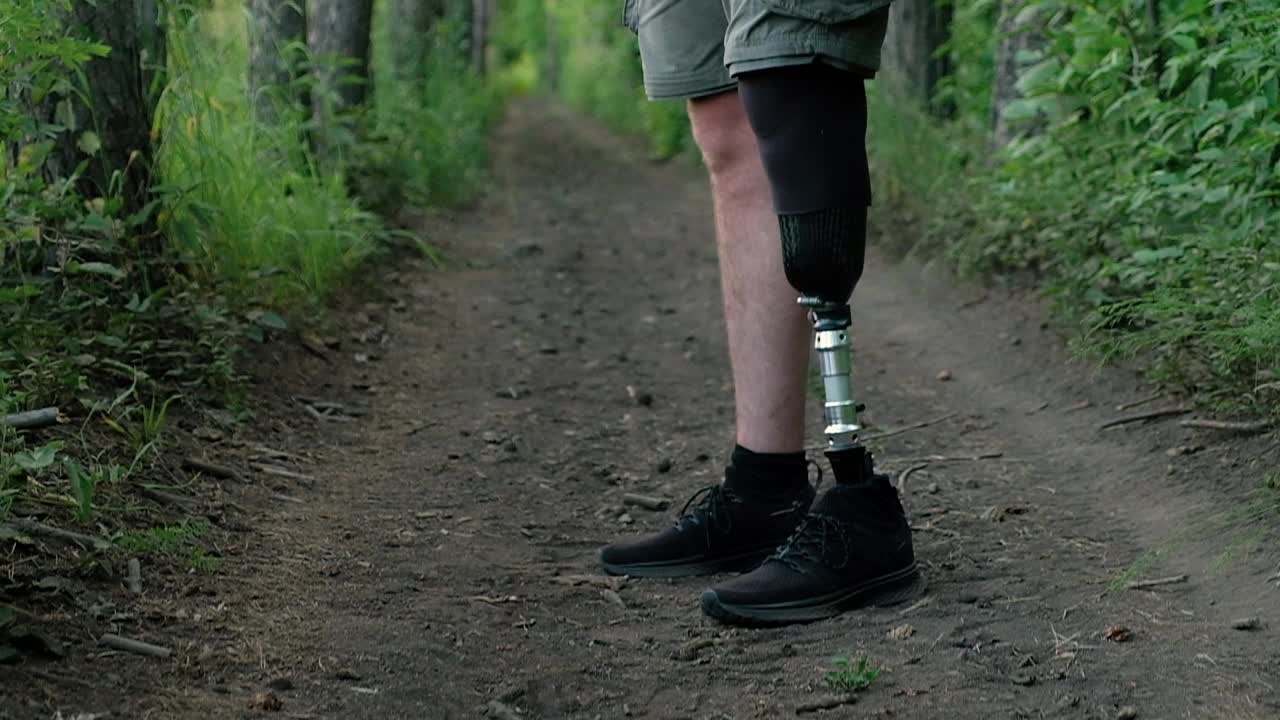 一名装着假腿的残疾人背着大背包，沿着森林小径行进视频下载