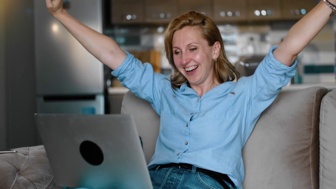 兴奋的女赢家用笔记本电脑庆祝在线成功坐在沙发上rbbro。快乐的女士视频素材