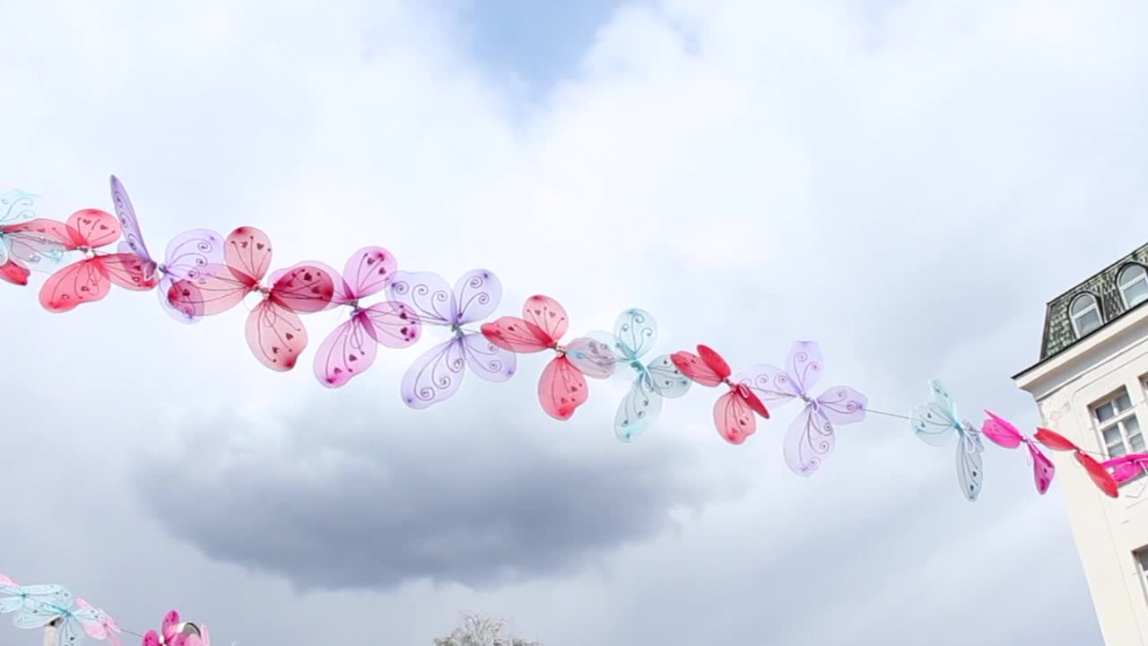 不同颜色的蝴蝶装饰挂在城市的一根绳子上视频下载