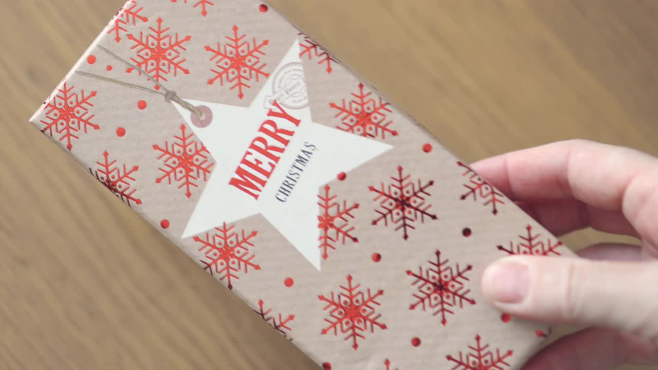 女手把写着“圣诞快乐”的红棕色工艺礼盒放在桌子上视频下载