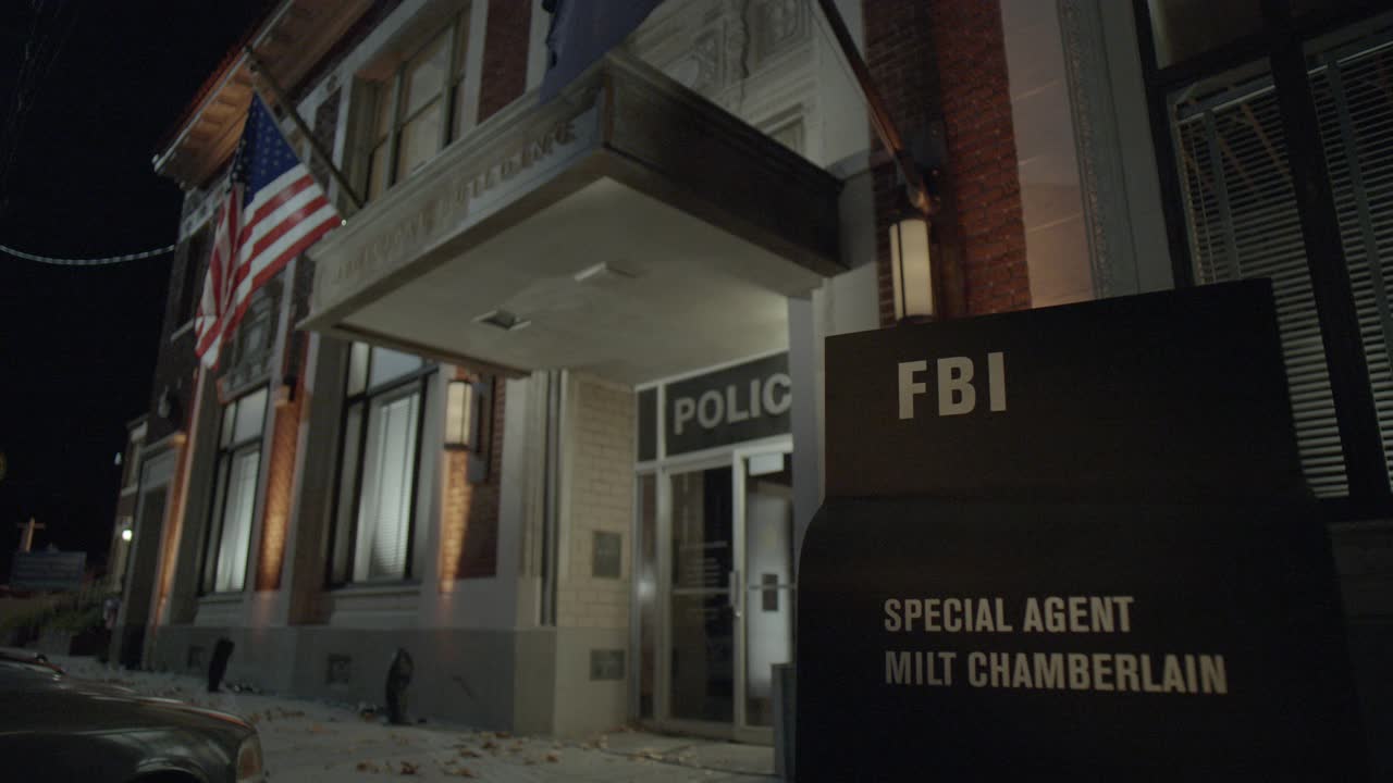 警察局入口的关闭角度。砖多层建筑。大楼前的招牌上写着"联邦调查局特工米尔特·张伯伦"。警察探员进入大楼。视频素材