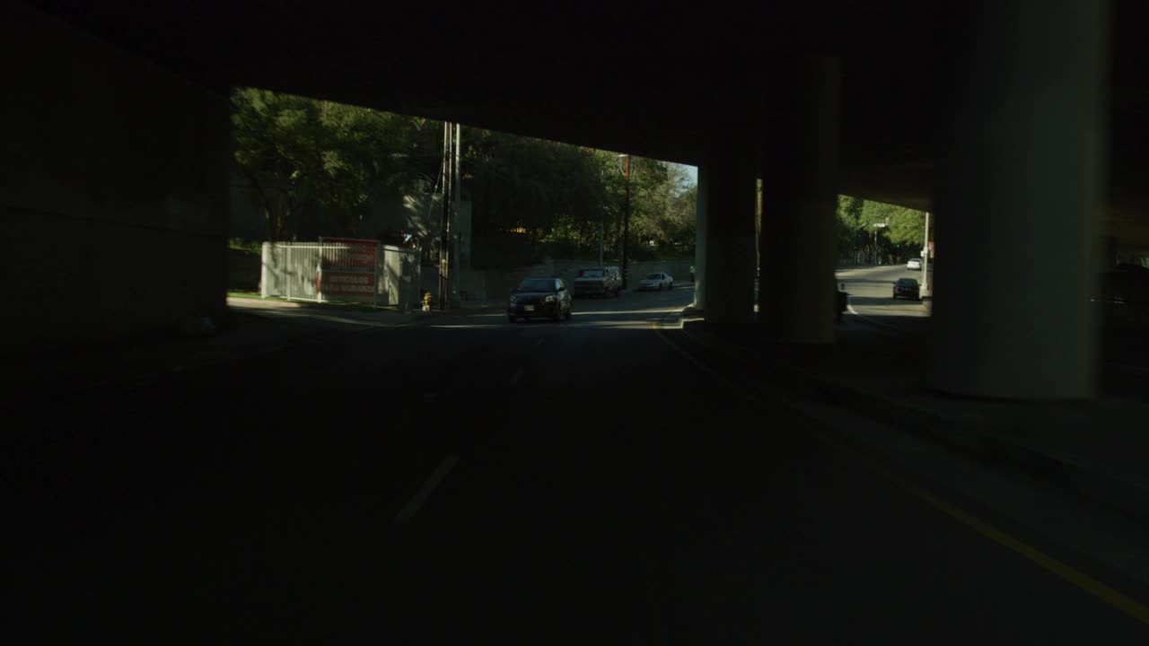 在城市街道上行驶的汽车的直背加工板。可以看到地下通道或桥梁、棕榈树、公寓楼、购物中心和企业。视频下载