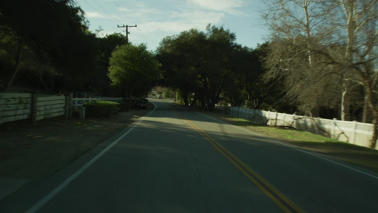 加工板直背的汽车行驶在农村地区或乡村道路上。树木、木栅栏和电线杆随处可见。房子或小牧场可见。可能是农场。可能是山路。视频素材