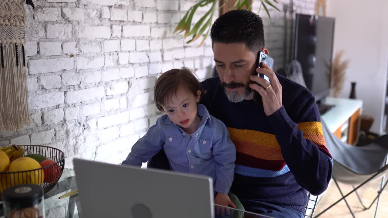 一个成熟的男人一边在家工作一边打电话，有特殊需要的儿子视频素材