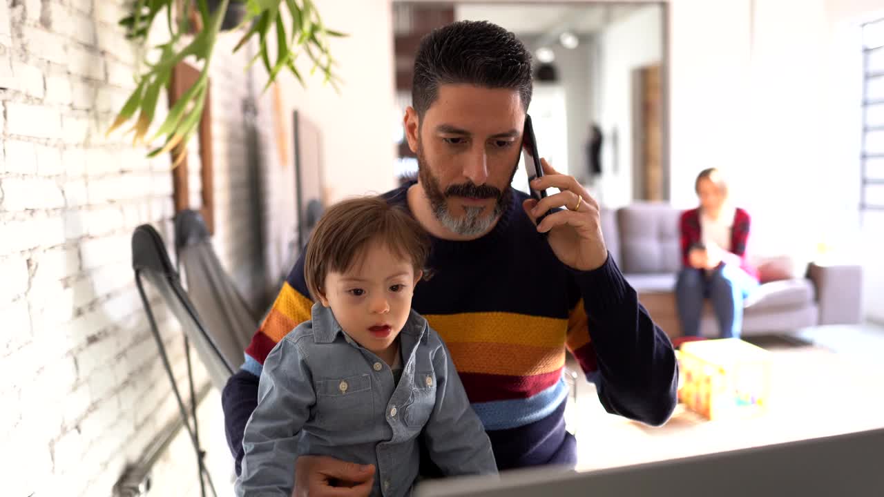 一个成熟的男人一边在家工作一边打电话，有特殊需要的儿子视频素材