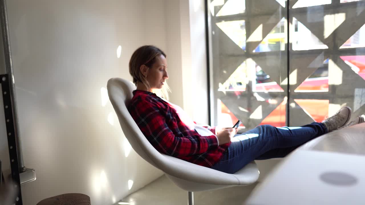 成熟的女人坐在窗台上用智能手机视频素材