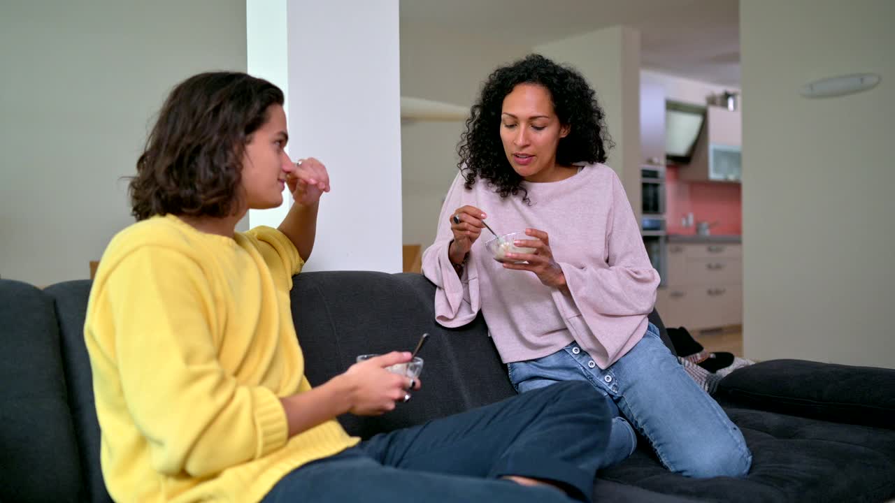 西班牙裔母亲和儿子在家里的沙发上吃冰淇淋和讨论视频素材