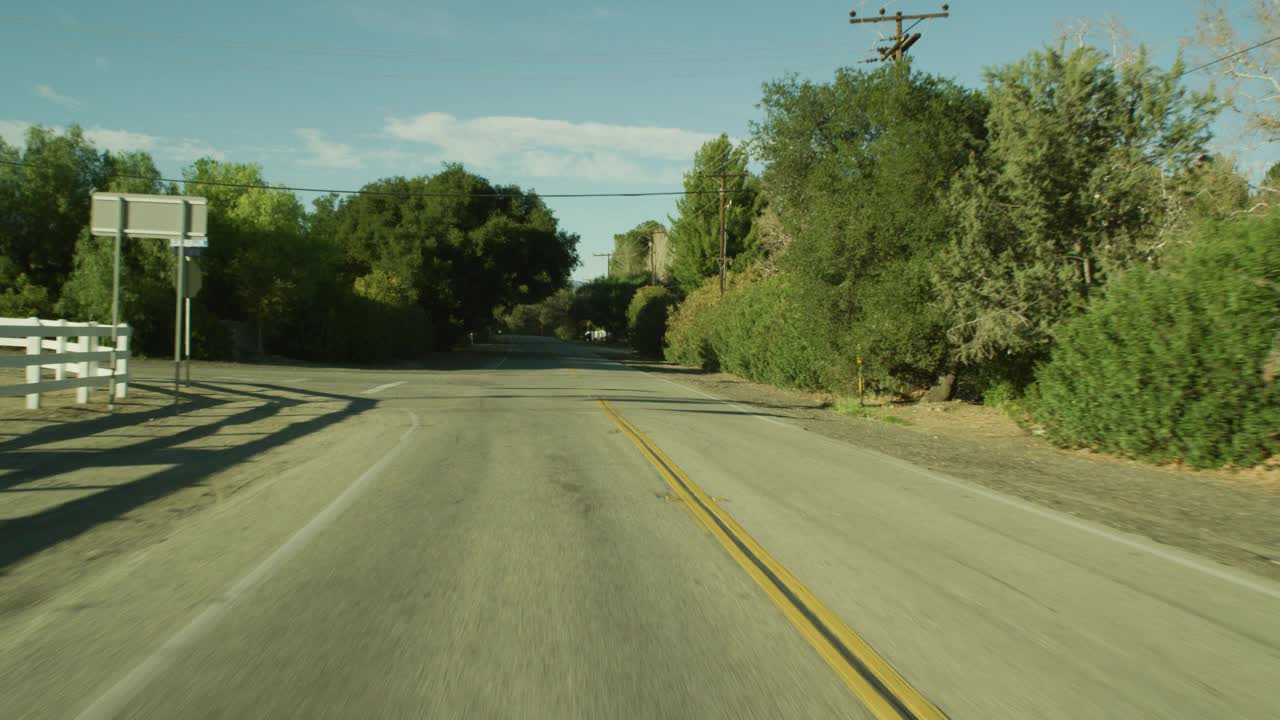 加工板直背的汽车行驶在农村地区或乡村道路上。树木、白色的篱笆和电线杆都清晰可见。可能是农田。可能是山路。视频素材