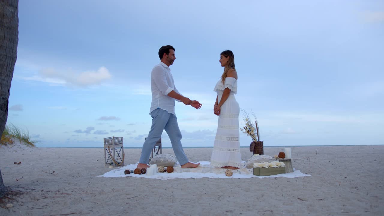 在浪漫的海滩野餐上，一个充满爱意的男人跪在地上问一个惊讶的女人是否愿意嫁给他视频下载