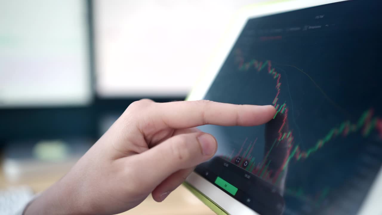 亚洲股票投资者穿着白色西装在卧室里看电脑屏幕和平板电脑上的股票图表。视频下载