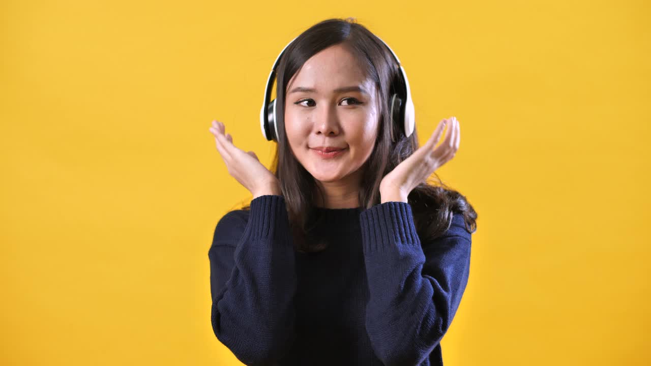 亚洲女人的肖像听音乐和跳舞孤立在演播室的黄色背景视频素材