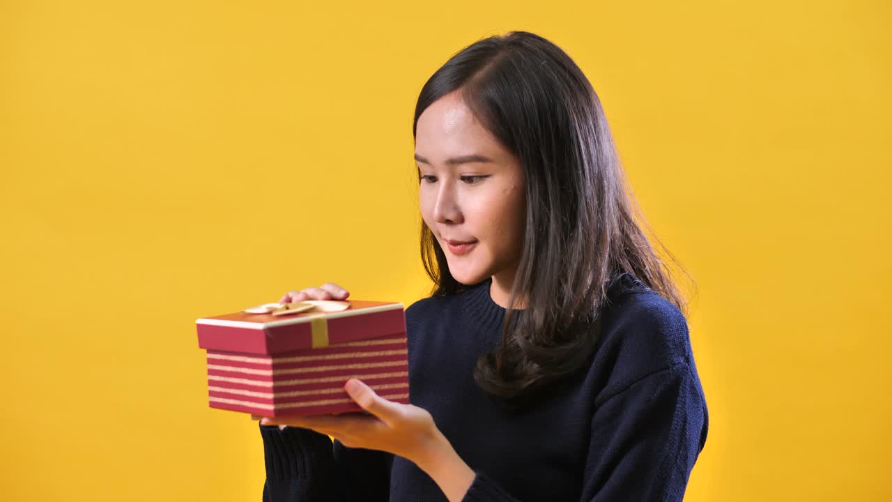 亚洲女人打开盒子在工作室的黄色背景视频下载
