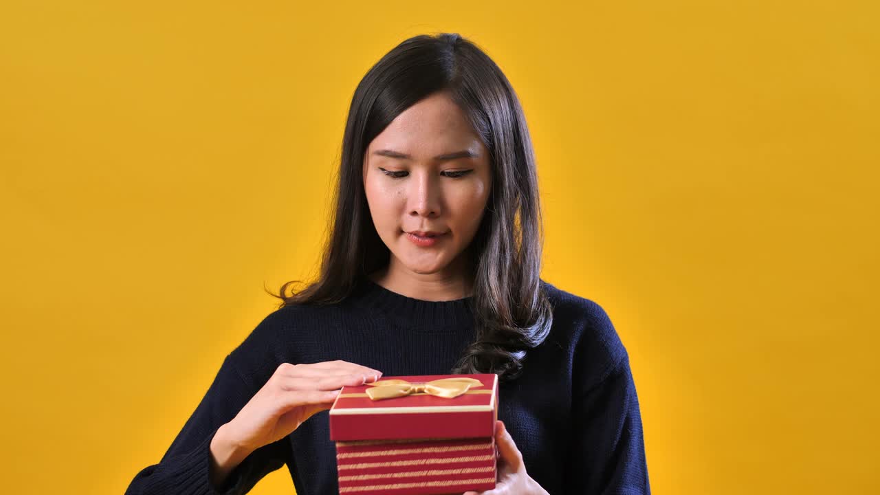 亚洲女人打开盒子在工作室黄色背景视频下载