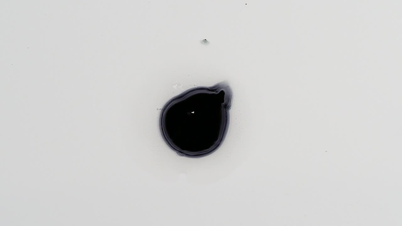 黑色颜料滴在空白画布上并展开的特写。视频下载